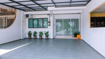 A covered outdoor area with a tiled floor, potted plants, and a window with blinds.