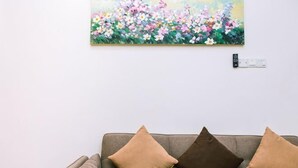 A gray sofa with two brown cushions against a white wall, a painting of flowers above it, and a power outlet to the right. - Karking 15@Pinjistation (8pax/4br) (Ipoh)