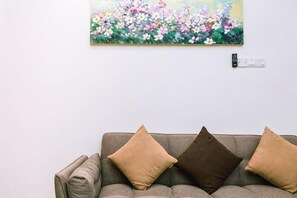 A gray sofa with two brown cushions against a white wall, a painting of flowers above it, and a power outlet to the right. - Karking 15@Pinjistation (8pax/4br) (Ipoh)