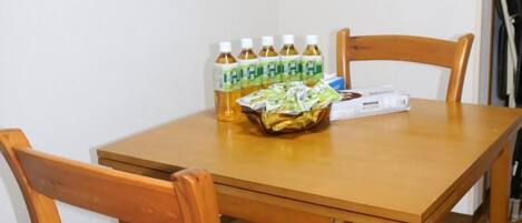A wooden dining table with a basket of snacks, several bottles of a beverage, and a box of tissues.