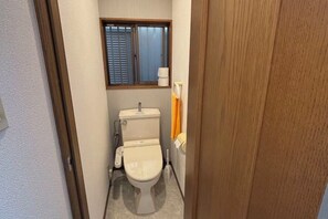 A small, compact bathroom with a toilet, a window, and a shower area. - XUYUAN (Osaka)