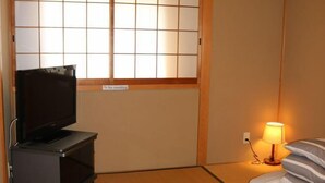 A hotel room with tatami flooring, a television on a stand, a bed with pillows, a nightstand with a lamp, and a shoji screen with a 'No smoking' sign. - XUYUAN (Osaka)
