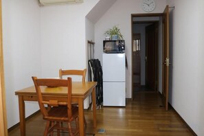 A small dining area with a wooden table and chairs, a white refrigerator, and a clock on the wall. - XUYUAN (Osaka)