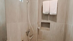 A shower area with a handheld showerhead and a towel rack with two towels. - Puri Residence Hotel (Sananwetan)