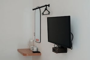 A wall-mounted TV, a mirror, and a small wooden shelf with a coffee maker and a cup.