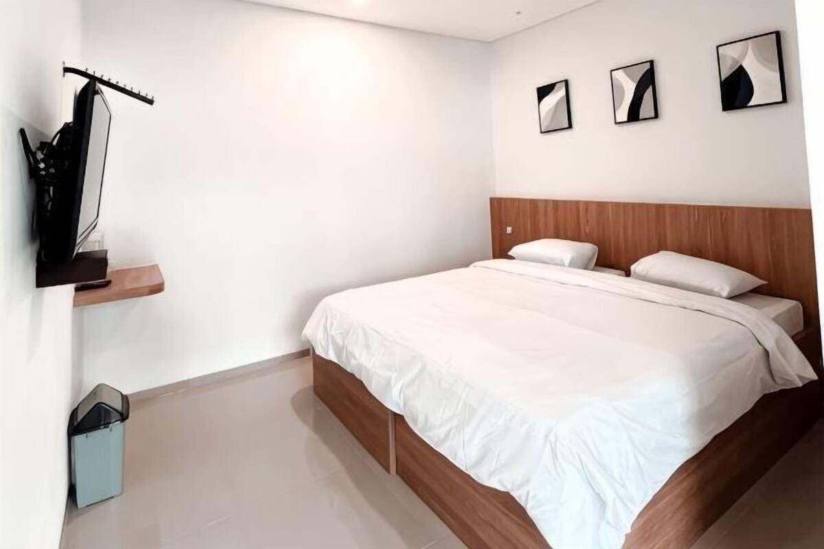 A bedroom with a bed, a wooden headboard, a wall-mounted guitar, and three framed pictures.