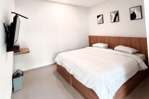 A bedroom with a bed, a wooden headboard, a wall-mounted guitar, and three framed pictures. - Puri Residence Hotel (Sananwetan)