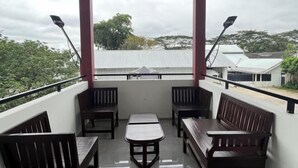 A balcony with wooden benches and a table, overlooking a residential area with houses and trees. - Puri Residence Hotel (Sananwetan)