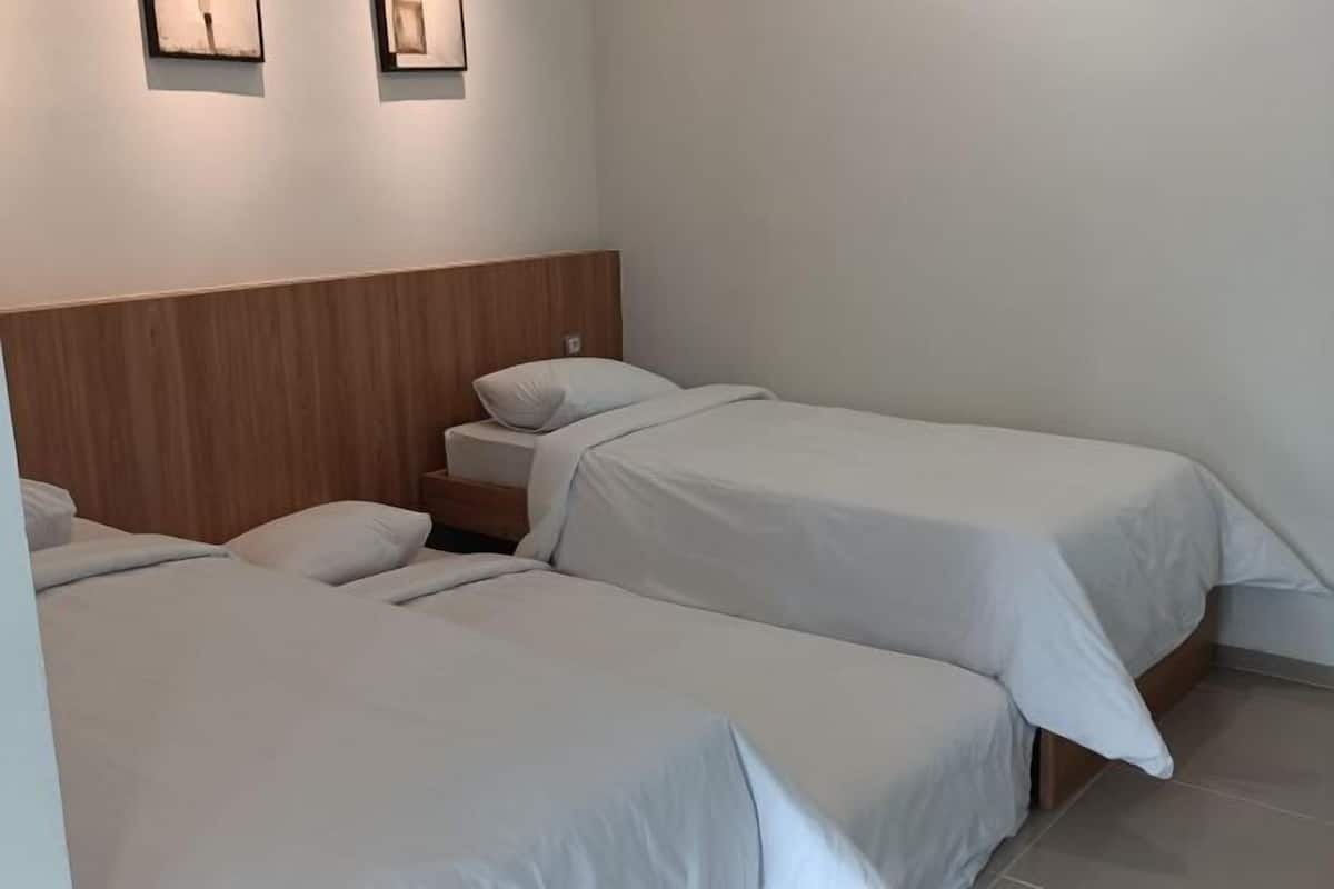 A hotel room with two single beds, a wooden headboard, and a nightstand with a lamp.