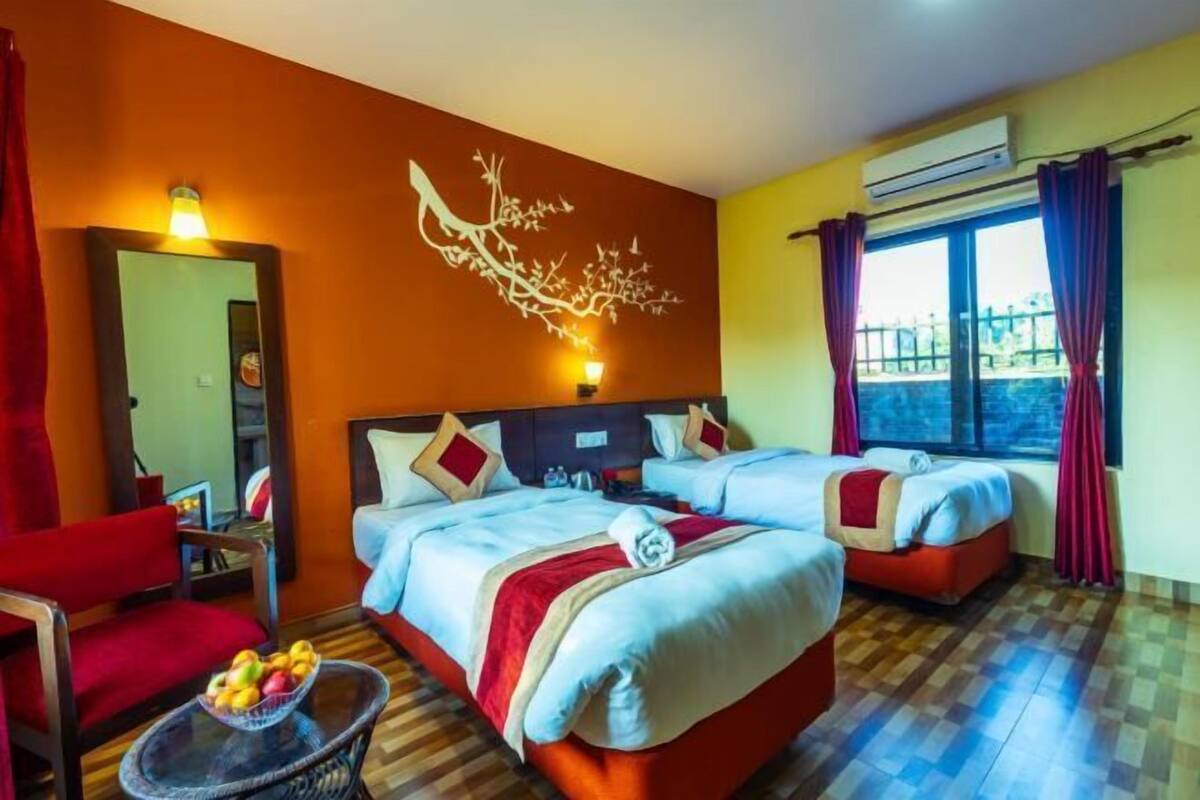Une chambre d’hôtel avec deux lits, une chaise rouge, une petite table avec des fruits et une fresque murale.