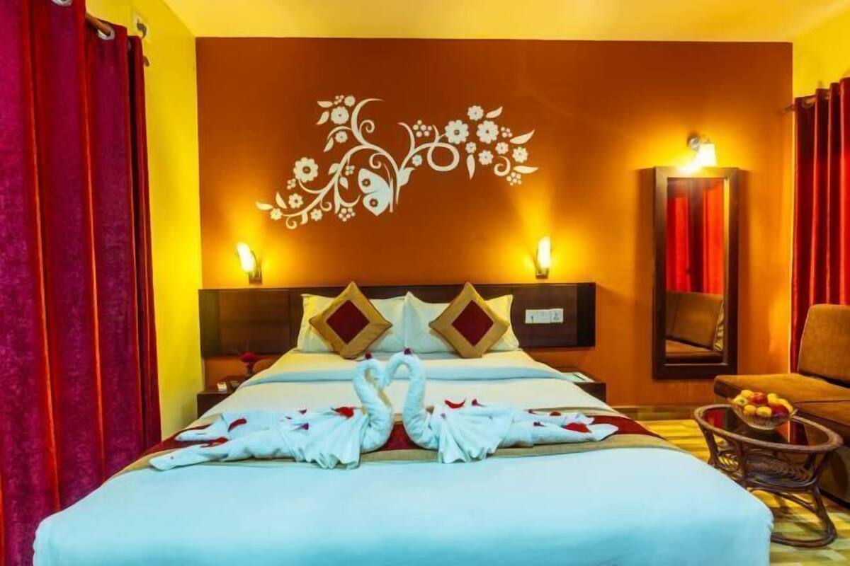 Une chambre d’hôtel comprenant un lit, un mur décoratif, une table de chevet, une chaise et un panier de fruits.
