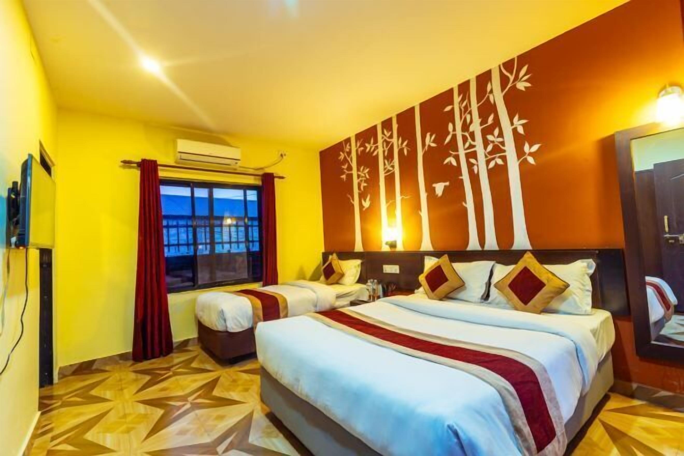 Une chambre d’hôtel avec deux lits, une grande fenêtre avec des rideaux, un téléviseur fixé au mur et un sol à motifs.