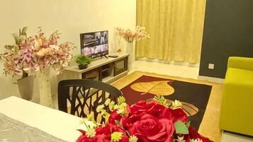 A dining area with a table, chairs, a vase of flowers, a television, and a yellow curtain.