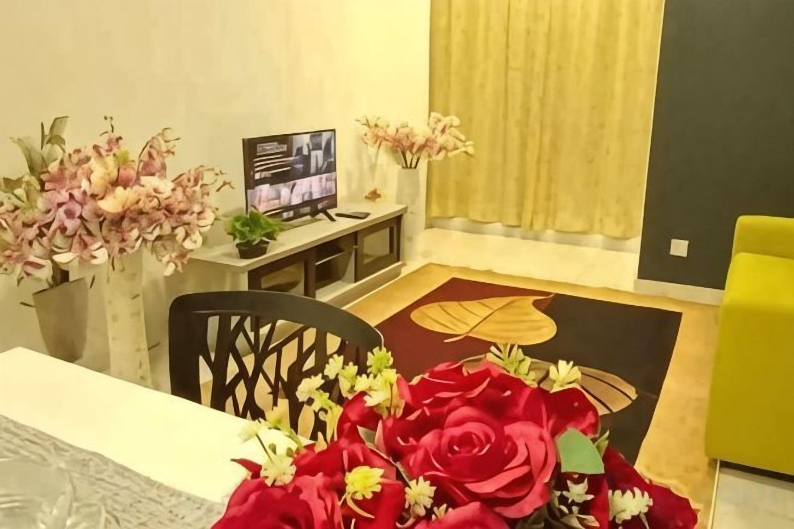 A living room with a TV, a dining table with a vase of flowers, and a yellow armchair.
