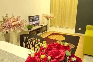 A room with a dining table, chairs, a TV, and a sofa. - The Transit Loft - Warisan StayHub (Dengkil)