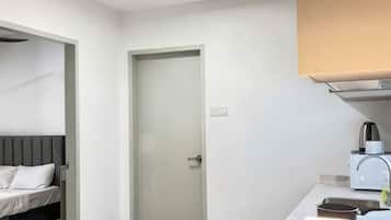 A small, modern room with a bed, a kitchenette, and a door.