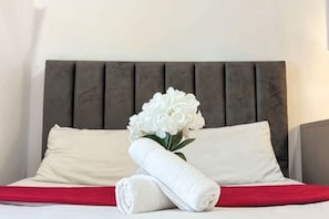 A neatly made bed with white linens, a red blanket, and a white flower arrangement. - The Transit Loft - Warisan StayHub (Dengkil)