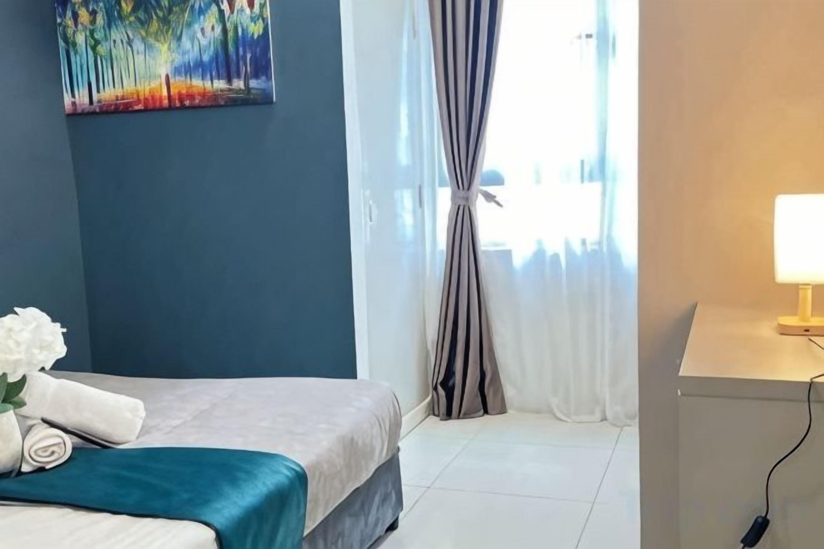 A hotel room with a bed, a desk, a lamp, and a painting on the wall.