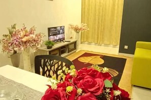 A dining area with a table, chairs, a TV, and flower arrangements. - The Transit Loft - Warisan StayHub (Dengkil)