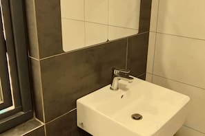 A bathroom with a white sink, dark tiled walls, and a window. - The Transit Loft - Warisan StayHub (Dengkil)