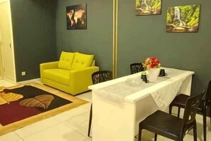 A room with a yellow sofa, a dining table with chairs, and artwork on the walls. - The Transit Loft - Warisan StayHub (Dengkil)