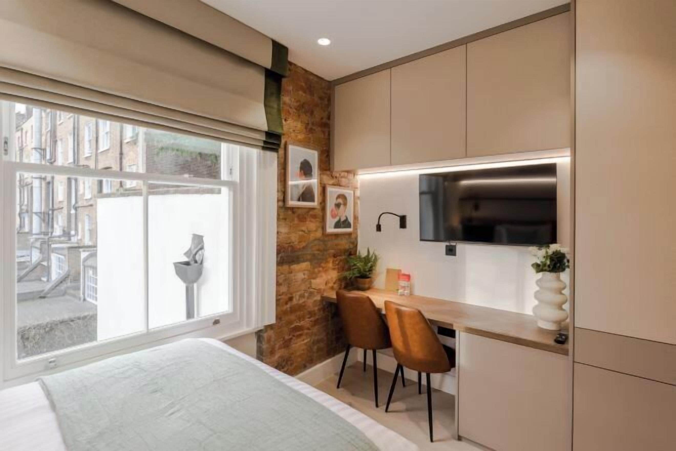 A modern bedroom with a large window, a bed, a small desk, and a stone accent wall.