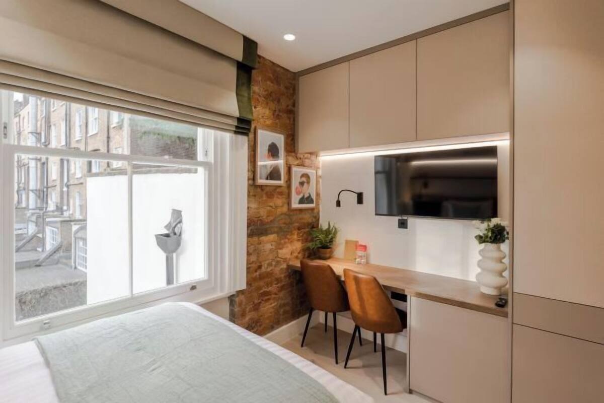 A modern bedroom with a large window, a bed, a small desk, and a stone accent wall.