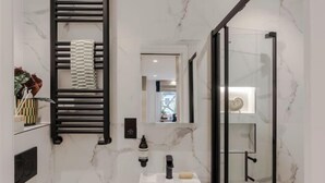 A modern bathroom with a white sink, black towel rack, and a glass shower enclosure. - Kensington Cosy Studio (London)