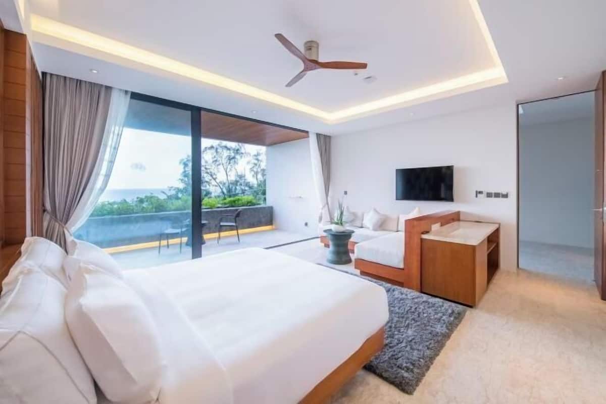 A modern hotel room with a large bed, a seating area with a view, a flat-screen TV, and a ceiling fan.