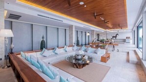A modern hotel lobby with a long sofa, a round coffee table, and a dining area with a wooden table and chairs. - Maya Anda Villa (Phuket)