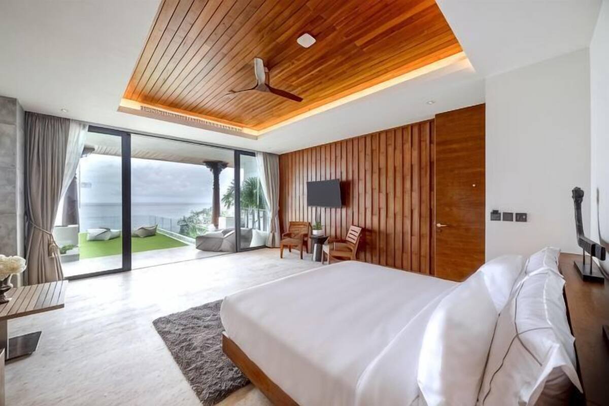 A bedroom with a large bed, a wooden ceiling, a TV, and a balcony with a view.