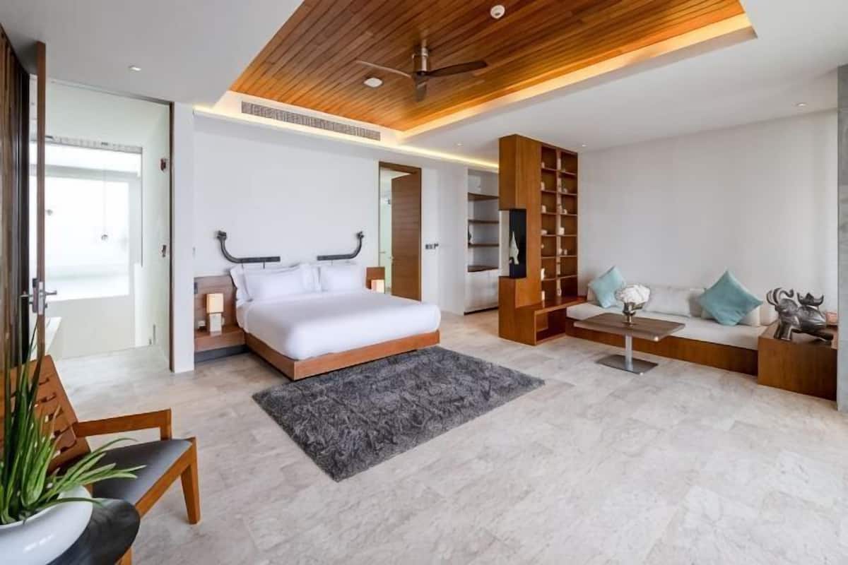 A modern bedroom with a large bed, a wooden ceiling, a built-in bookshelf, and a seating area with a sofa and coffee table.