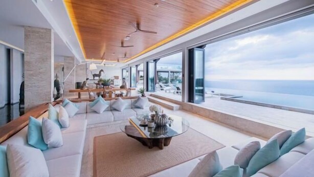 Ein modernes Interieur mit einem großen Panoramafenster mit Meerblick, einer Holzbalkendecke und einer Sitzecke mit Couchtisch.