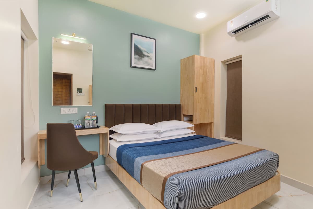 A bedroom with a bed, a desk, a chair, a wardrobe, and an air conditioner.