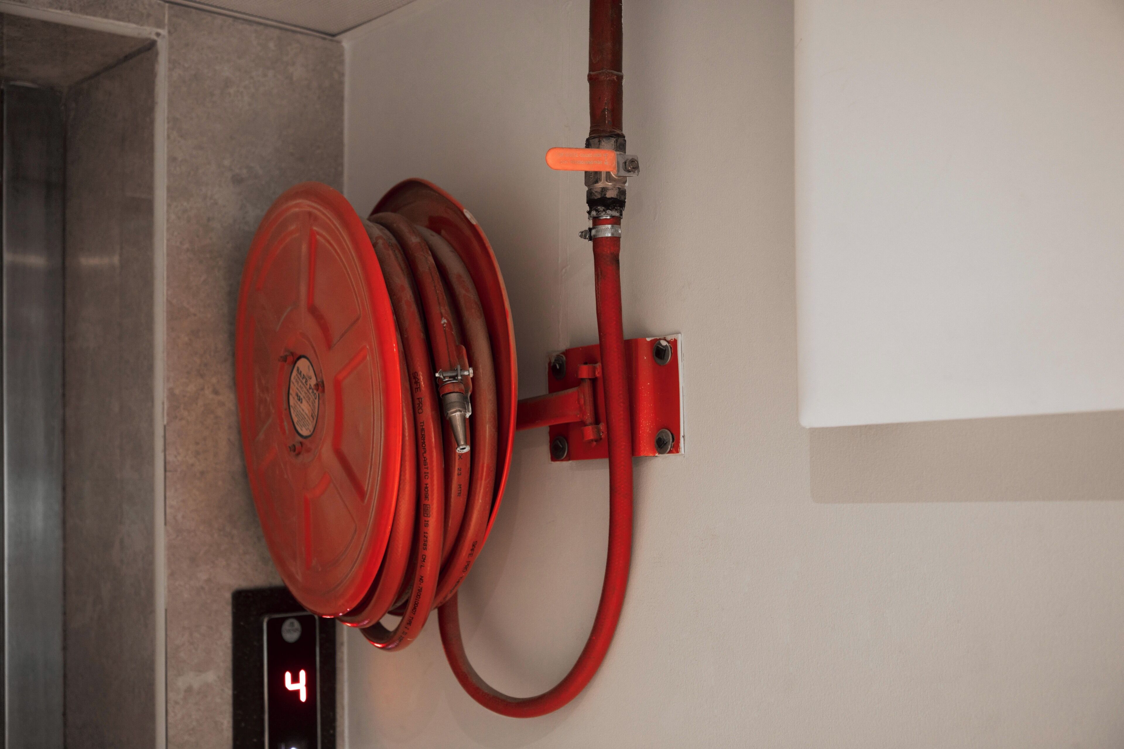 Una manguera roja enrollada en una pared, junto a un panel de alarmas contra incendios.