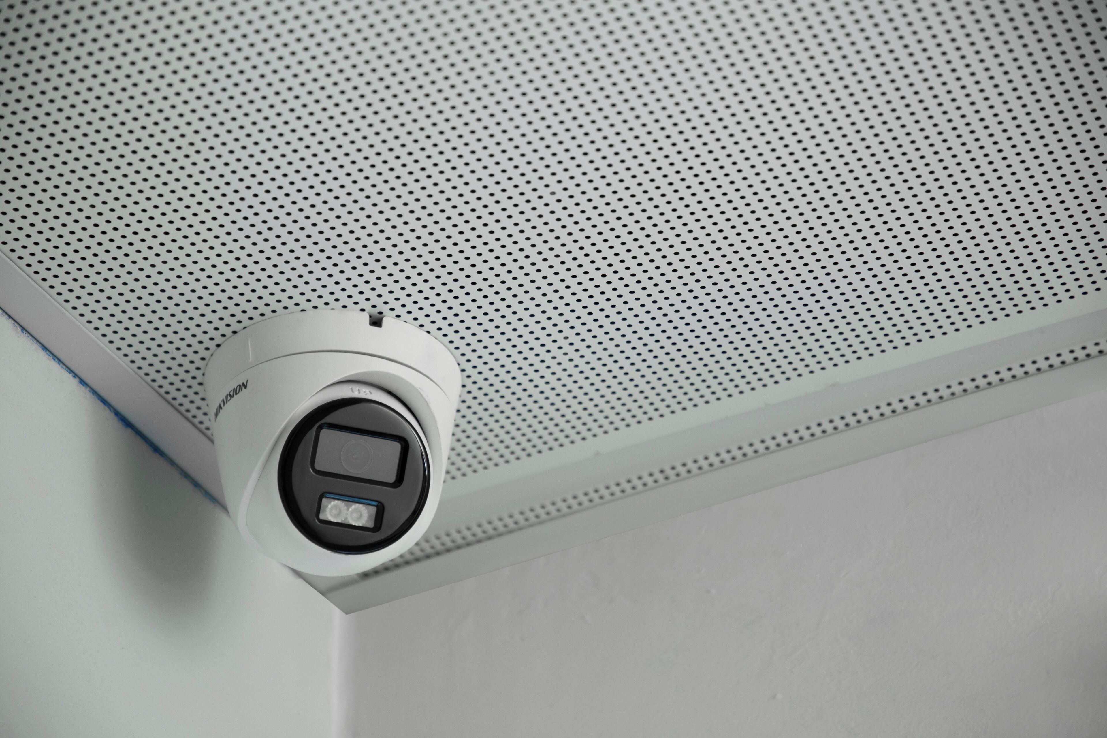 A security camera mounted on a ceiling with a perforated pattern.