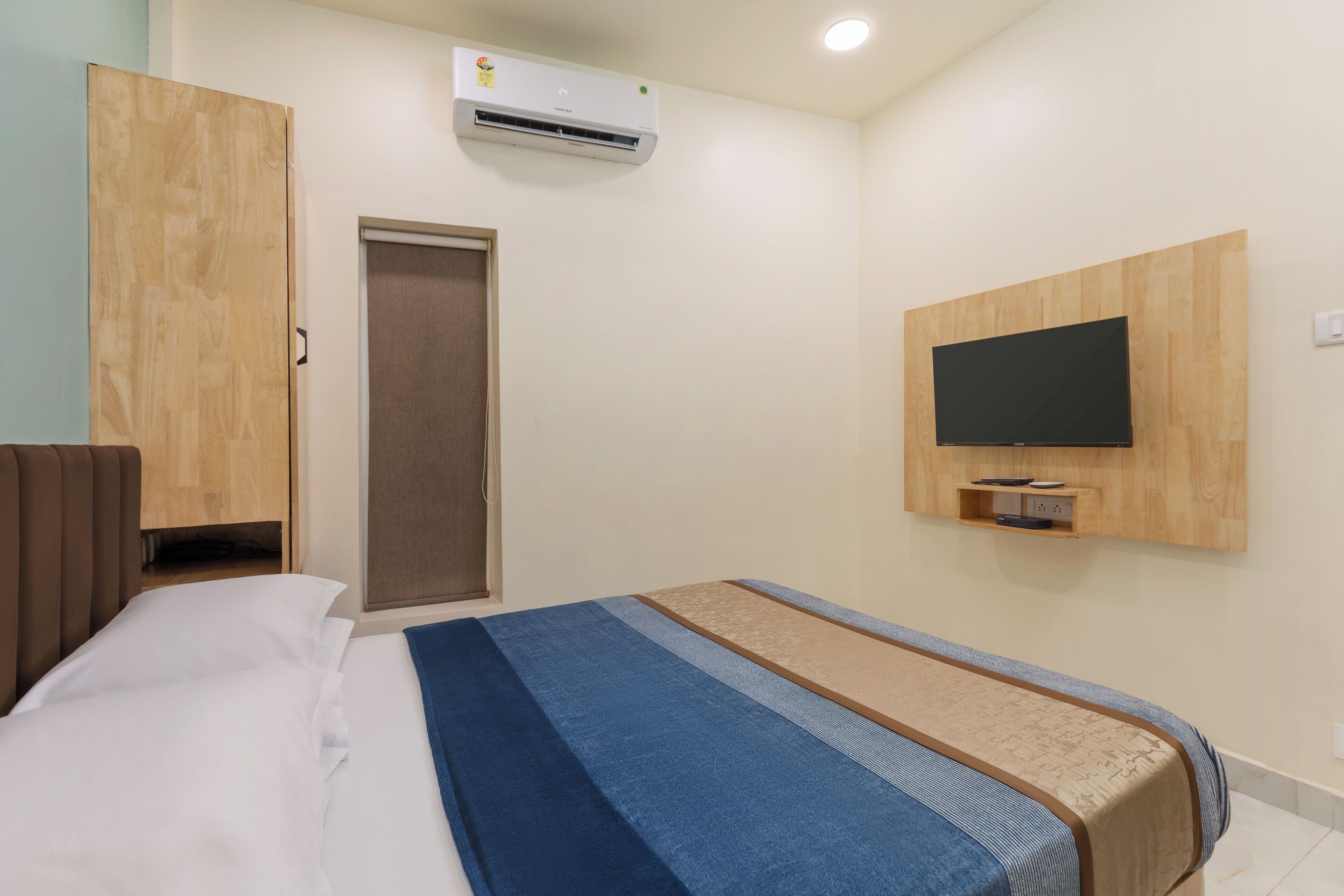 Una habitación de hotel con cama, armario, televisor montado en la pared y aire acondicionado.