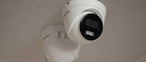 A white security camera mounted on a ceiling with a perforated pattern.