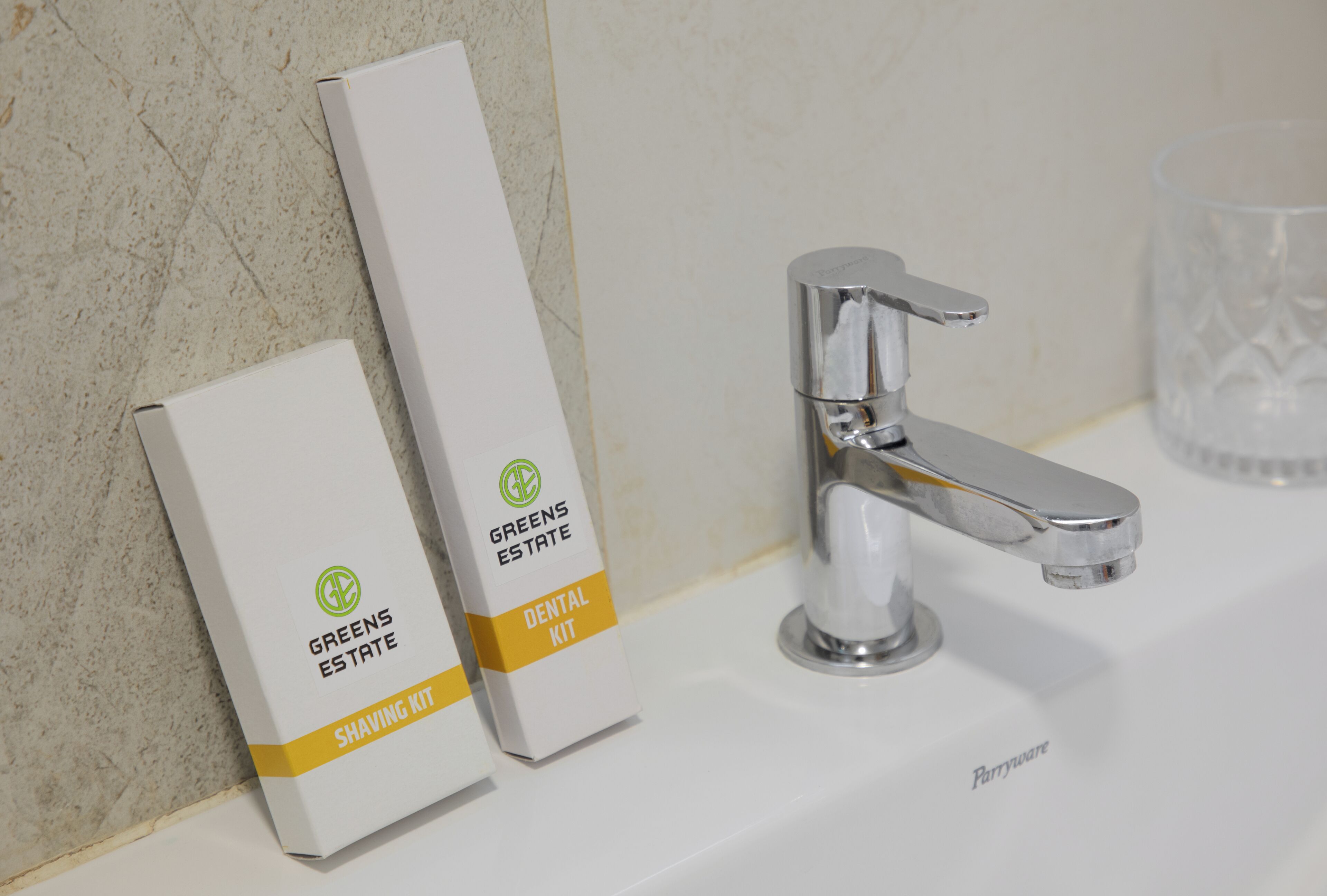 Een badkamer met een witte wasbak, een chromen kraan en twee dozen met de tekst 'Greens Estate Shaving Kit' aan de muur.