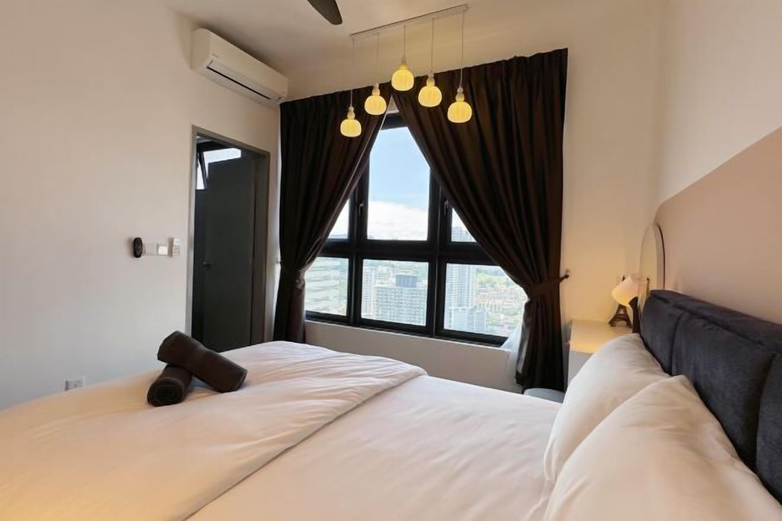 A hotel room with a bed, a window with curtains, a ceiling fan, and a view of the city.