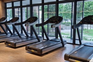 Four treadmills arranged in a row with a view of greenery outside through large windows. - M Vertica KL City 4 Bedroom Fully Air-Con Suite (Kuala Lumpur)
