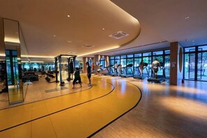 A gym with cardio equipment, mirrors, and a curved wooden floor. - M Vertica KL City 4 Bedroom Fully Air-Con Suite (Kuala Lumpur)
