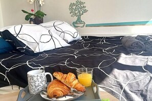 A neatly made bed with a black and white patterned bedspread, a plate with croissants and orange juice, and a floral mug on a tray. - New Studio/Near Airport CDG/Direct Paris center/Disneyland/Villepinte EXPO (Tremblay En France)