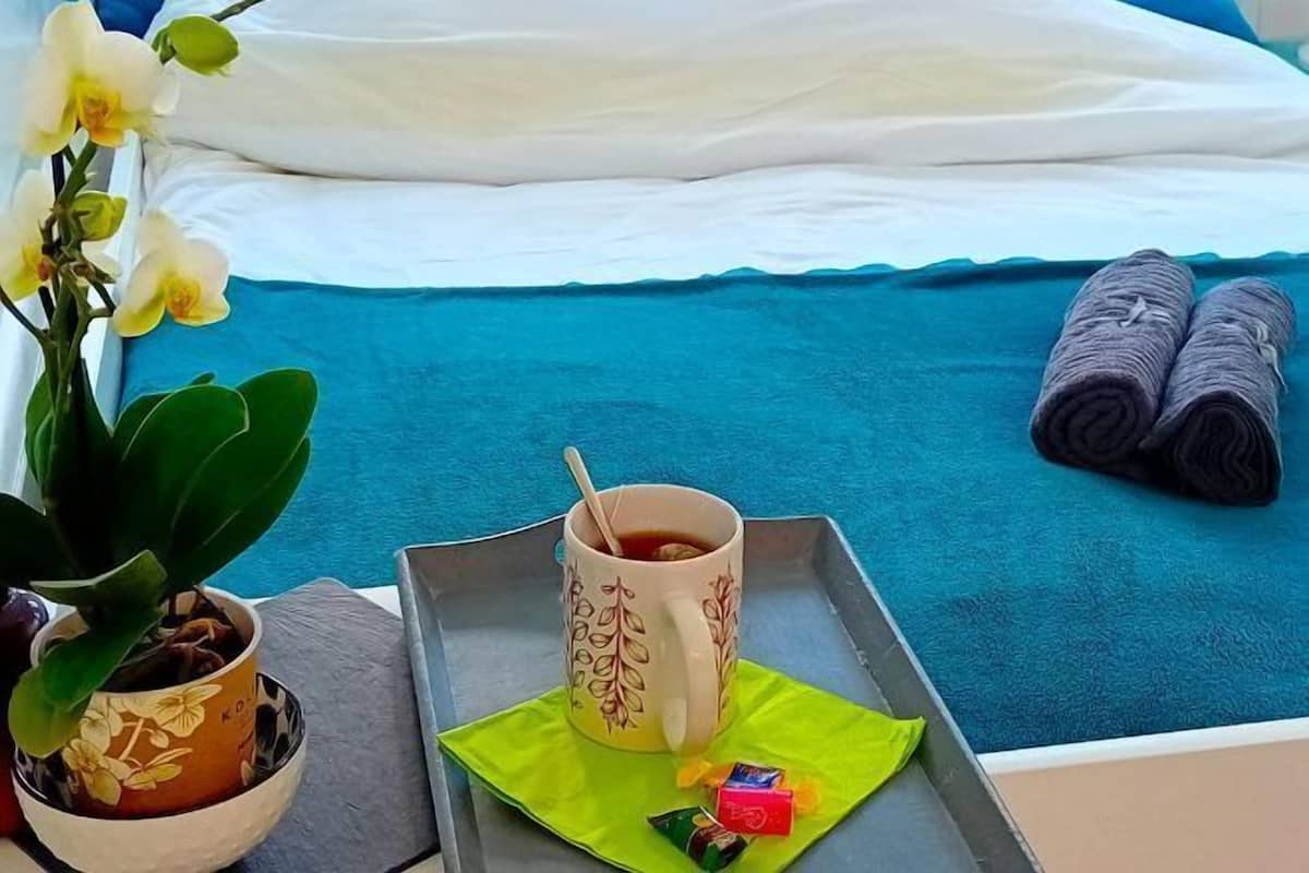 Ein ordentlich bezogenes Bett mit einer blauen Bettdecke, einem weißen Kopfkissen und einem Paar zusammengerollter Handtücher.