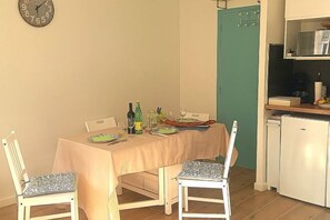 A dining area with a table set for two, chairs, a clock on the wall, and a kitchen area with a refrigerator and microwave. - New Studio/Near Airport CDG/Direct Paris center/Disneyland/Villepinte EXPO (Tremblay En France)