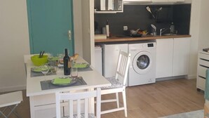 A compact kitchen with a washing machine, a dining table with chairs, and a teal door. - New Studio/Near Airport CDG/Direct Paris center/Disneyland/Villepinte EXPO (Tremblay En France)