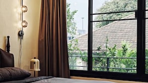 A hotel room with a bed, a nightstand, a wall-mounted light fixture, and a view of greenery outside. - 4Br Modern Art Villa with Free Wi-Fi Netflix Vinyl (Bangkok)