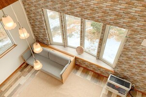 Ein Zimmer mit Backsteinwand, großen Fenstern, einer Couch und hängenden Lampen.