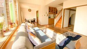 A modern living room with a sofa, a dining table, and a kitchen area in the background. - Pokke (Shiraoi)