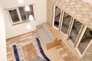 A room with a sofa, a wooden coffee table, and a large window with a view.